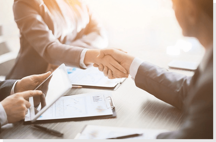 Two people shaking hands over a table.