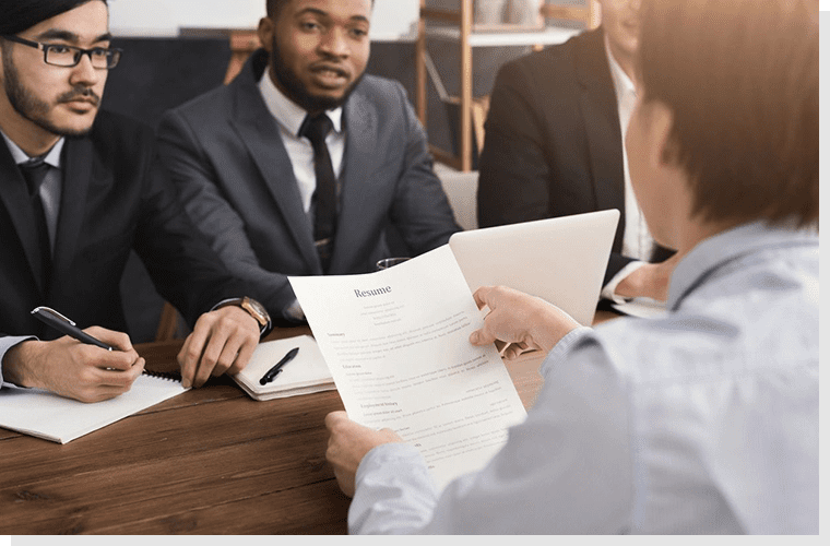 A man is holding papers while two other men are sitting at the table.